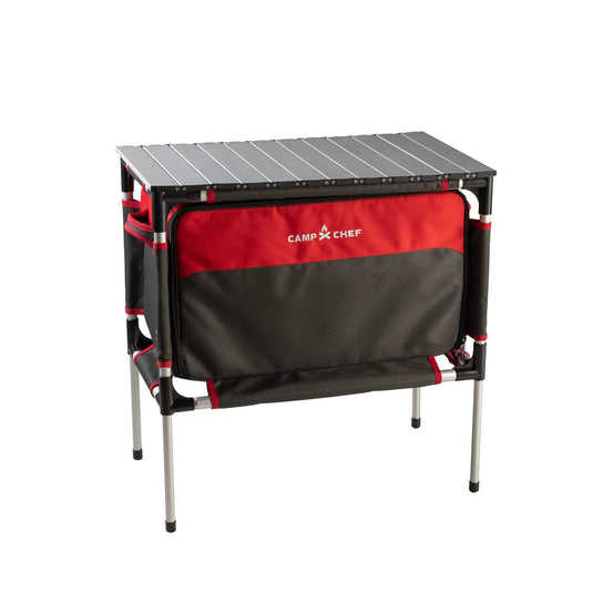 The Camp Chef Sherpa Table & Organizer features a black tabletop, silver legs, and a black and red zippered storage compartment—perfect for use as a portable camp table or organizer on your outdoor adventures.