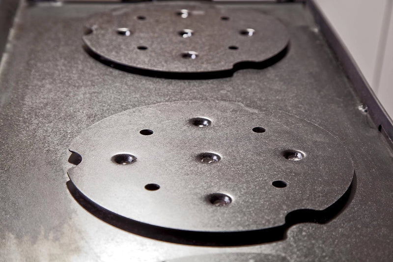Load image into Gallery viewer, Close-up of two round metal stove plates with holes and notches, placed on a cast iron stove—perfect for using the Camp Chef Griddles 14 as a flat top griddle or heat diffuser plate.

