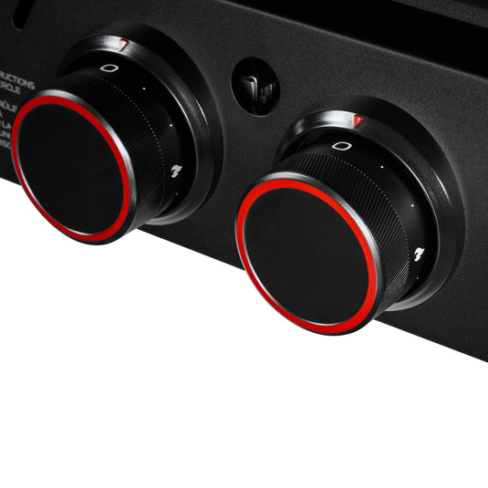 Close-up of two black control knobs with red accents on the Camp Chef Gridiron Gameday outdoor cooking system. The knobs have white indicator markings and symbols, set against a sleek black surface.