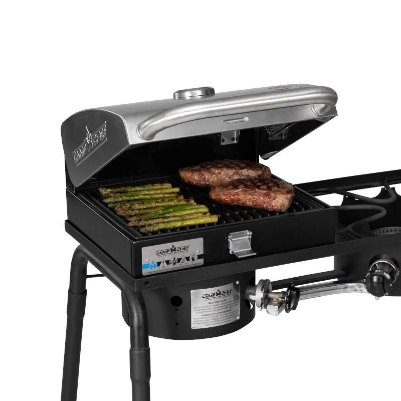 Load image into Gallery viewer, The Camp Chef BBQ Grill Boxes 14, shown with its lid open, cooks asparagus and two steaks on a cast iron surface. This black grill features a metal lid, heat diffuser system, and side burner for versatile outdoor cooking.
