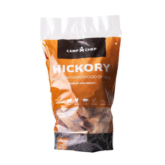 A clear, orange Camp Chef bag labeled Wood Chunks contains hardwood pieces for grilling and smoking. The package features food icons and text about a robust, smoky flavor—ideal for any hardwood grill.