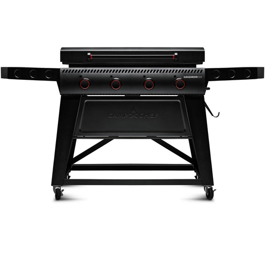 The Camp Chef Gridiron 36 is a black outdoor gas grill featuring four control knobs, foldable side shelves, a closed lid, and wheels for mobility, providing even heating and easy clean-up.