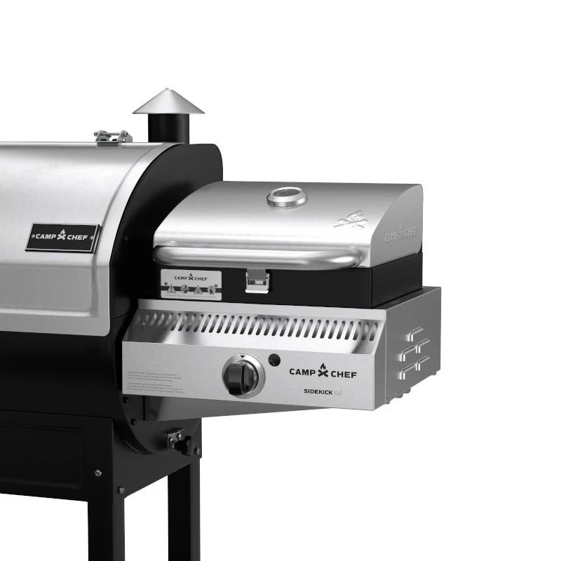 Load image into Gallery viewer, A close-up of a Camp Chef grill with the Camp Chef Sidekicks accessory, showing a stainless steel propane burner control knob and a small chimney vent on the main grill.
