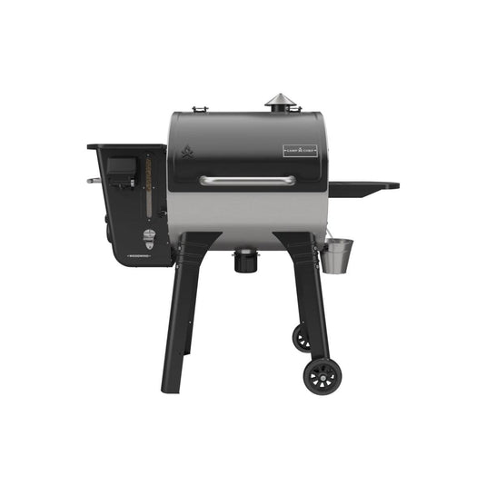 The Camp Chef Woodwind 24 is a black and silver pellet grill with a barrel-shaped body, WIFI controller on the left panel, chimney on top, right-side shelf, and two wheels for easy mobility.