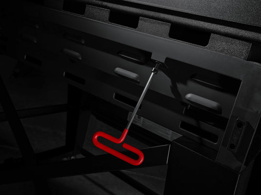 A close-up of the Camp Chef Gridiron 36 showcases a red-handled tool in the side slot, highlighted against the sleek black griddle for convenient clean-up after even heating.