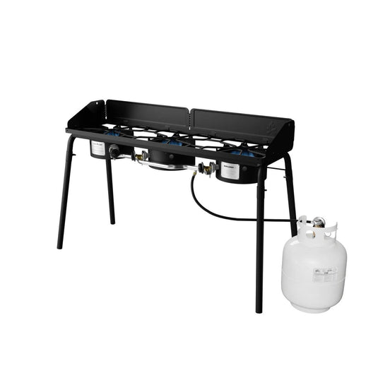 The Camp Chef Explorer is a black metal cooking system with two burners, four legs, control knobs, and a connected white propane tank—ideal for outdoor cooking or camping.
