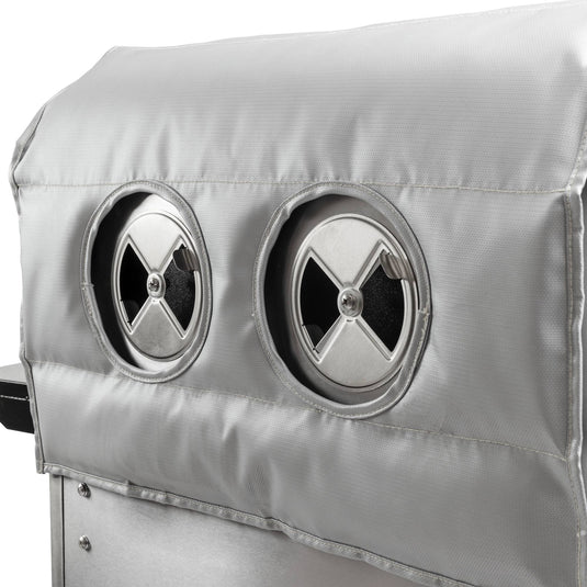 Close-up of a Camp Chef Woodwind Pro Blanket, a silver fire-resistant fiberglass cover for Woodwind grills, featuring two circular vents with adjustable cross-shaped openings.