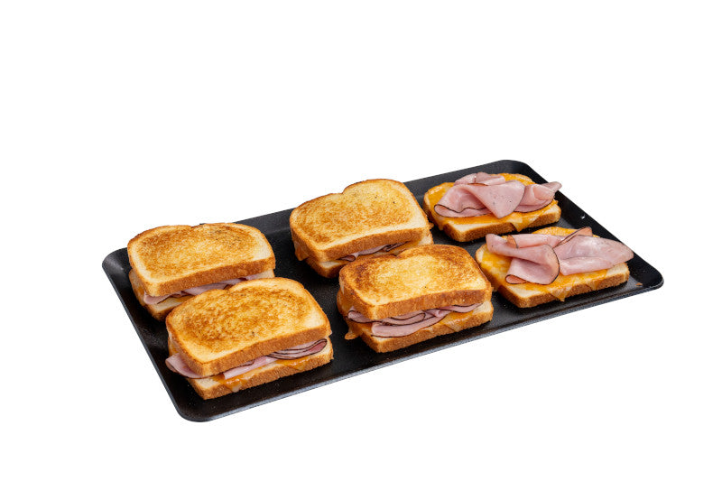 Load image into Gallery viewer, A black tray displays six grilled ham sandwiches—four with golden toasted tops and two open-faced—freshly made on the Camp Chef Compact Stove Griddle, set against a white background.
