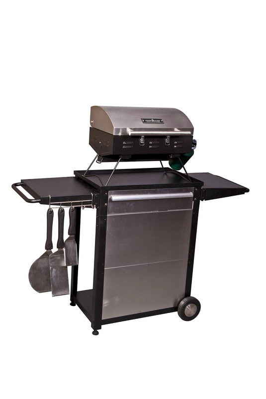 The Camp Chef Patio Cart is a stainless steel outdoor gas grill with a closed lid, side shelves, two wheels, and barbecue tools hanging on the left—ideal as an outdoor kitchen cart—shown isolated on a white background.