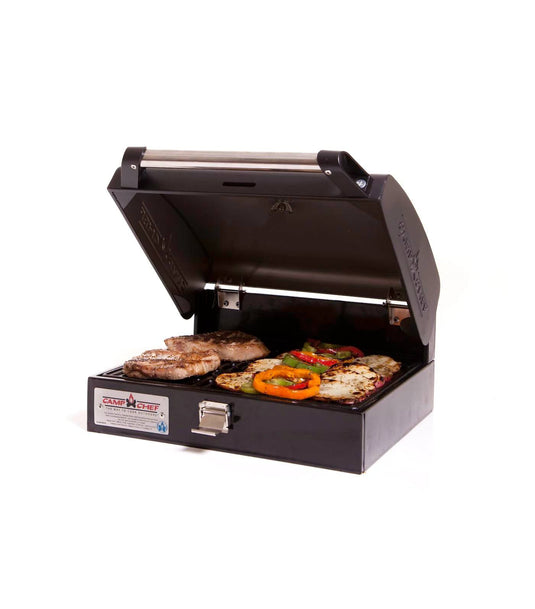 With its lid open, the Camp Chef BBQ Grill Boxes 14 cooks steaks, peppers, zucchini, and mushrooms on a cast iron surface. This compact black grill is perfect for at-home or outdoor use and sits on a white background.