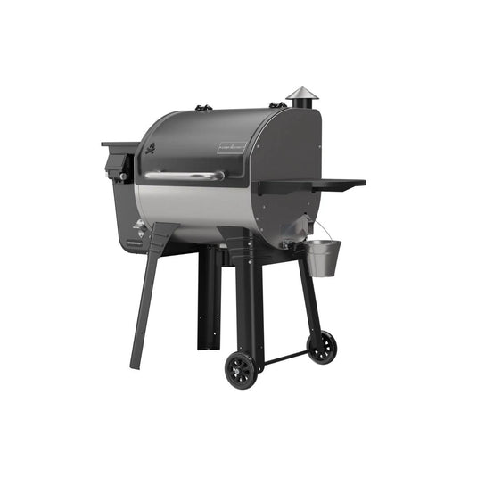 The Camp Chef Woodwind 24 is a black and silver, barrel-shaped pellet grill smoker featuring WIFI control, a chimney, side shelf, wheels for mobility, and a small metal bucket underneath for grease collection.