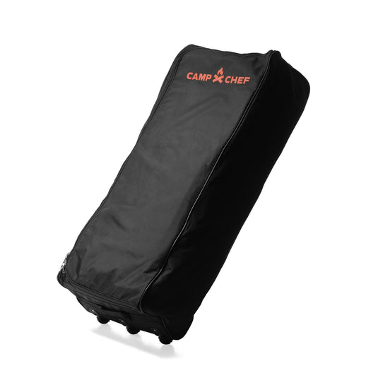 The Camp Chef Stove System Roller Bag is a black, heavy-duty carry bag with wheels and a red Camp Chef logo on top. It stands upright, features durable padded fabric, and is perfect for carrying your Camp Chef 2-burner stove.